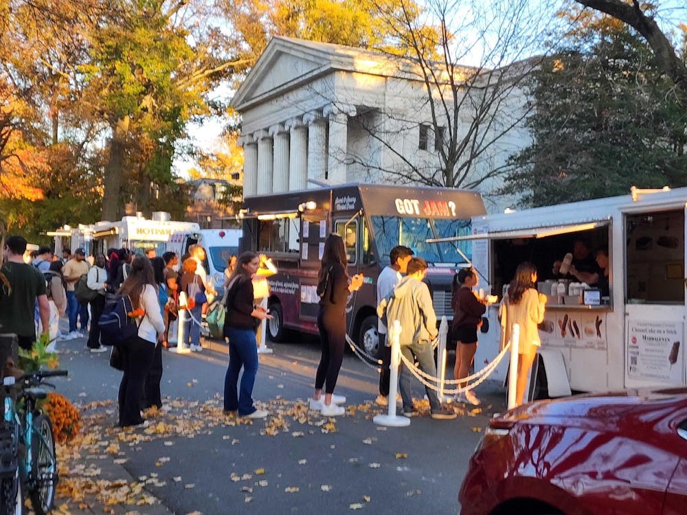 A line of students in front of Whig Hall waiting for a food truck. In the background, two more trucks, also with lines.