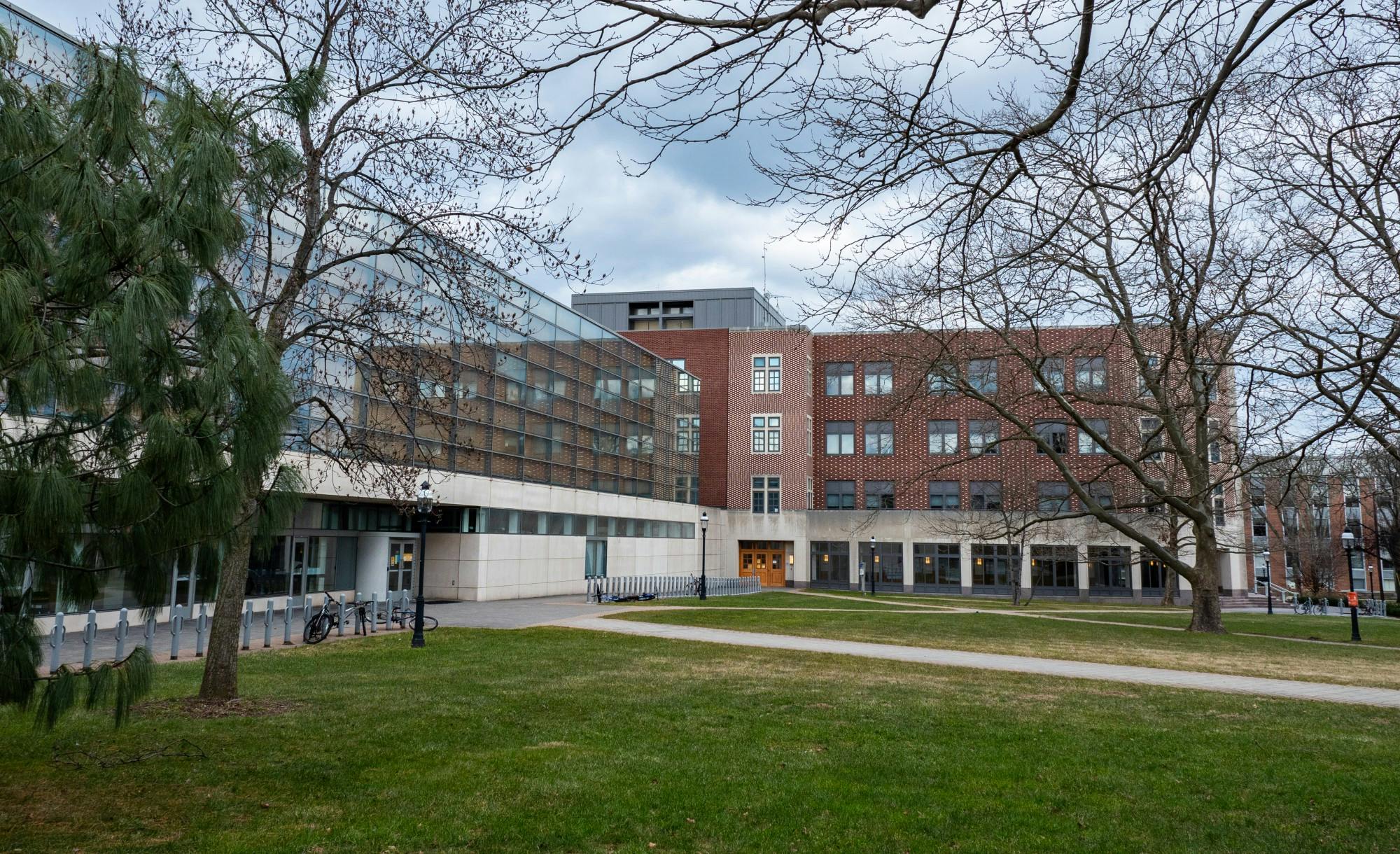 a white building with lots of windows, in front of a brick building, with a grassy area in front of it. 
