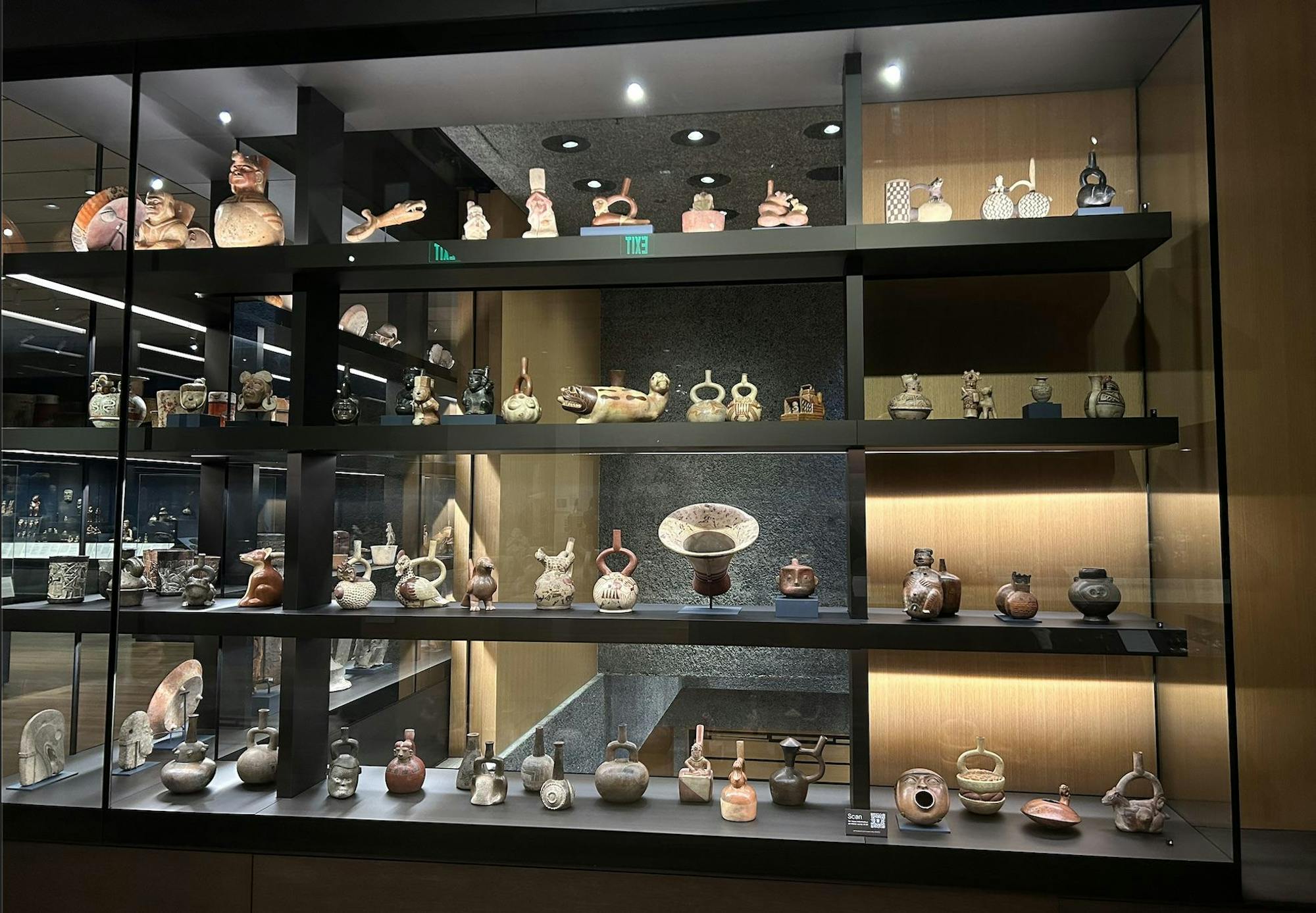 5 shelves of various ceramic objects including bowls, vases, and other objects encased in glass. 