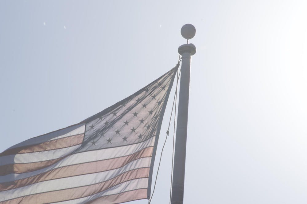 An American flag flying in the wind attached to a flag pole in front of a blue sky.