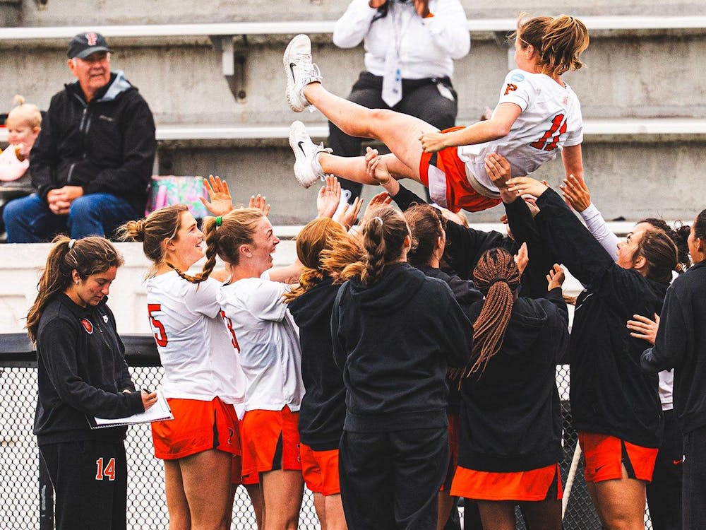 Lacrosse players in white and orange jerseys celebrating, lifting a player in the air.