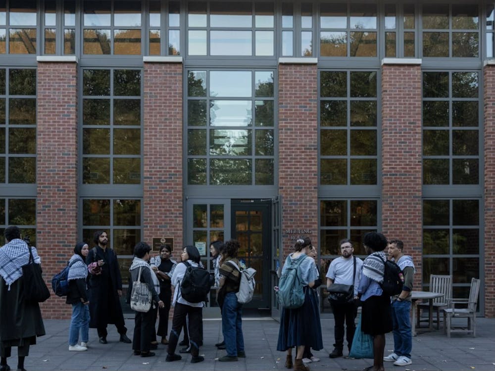 Small group of individuals wearing keffiyehs gather outside, courthouse looms in the background.