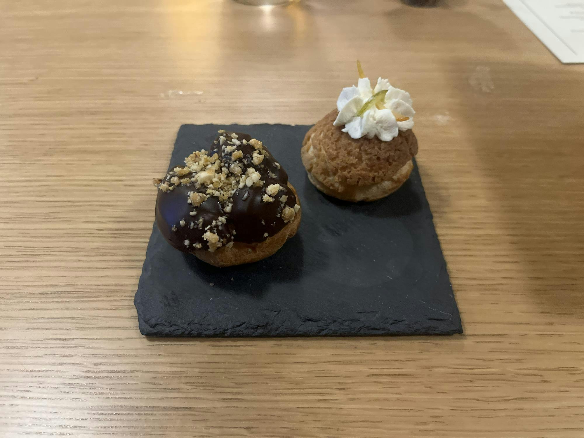 Two tan pastries, one with a black sauce and one with a white dollop of cream.