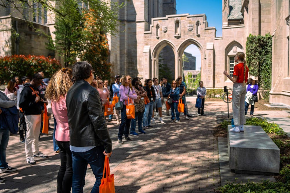 Bright day in courtyard. Someone in orange shirt standing atop stone speaking to crowd on the left.