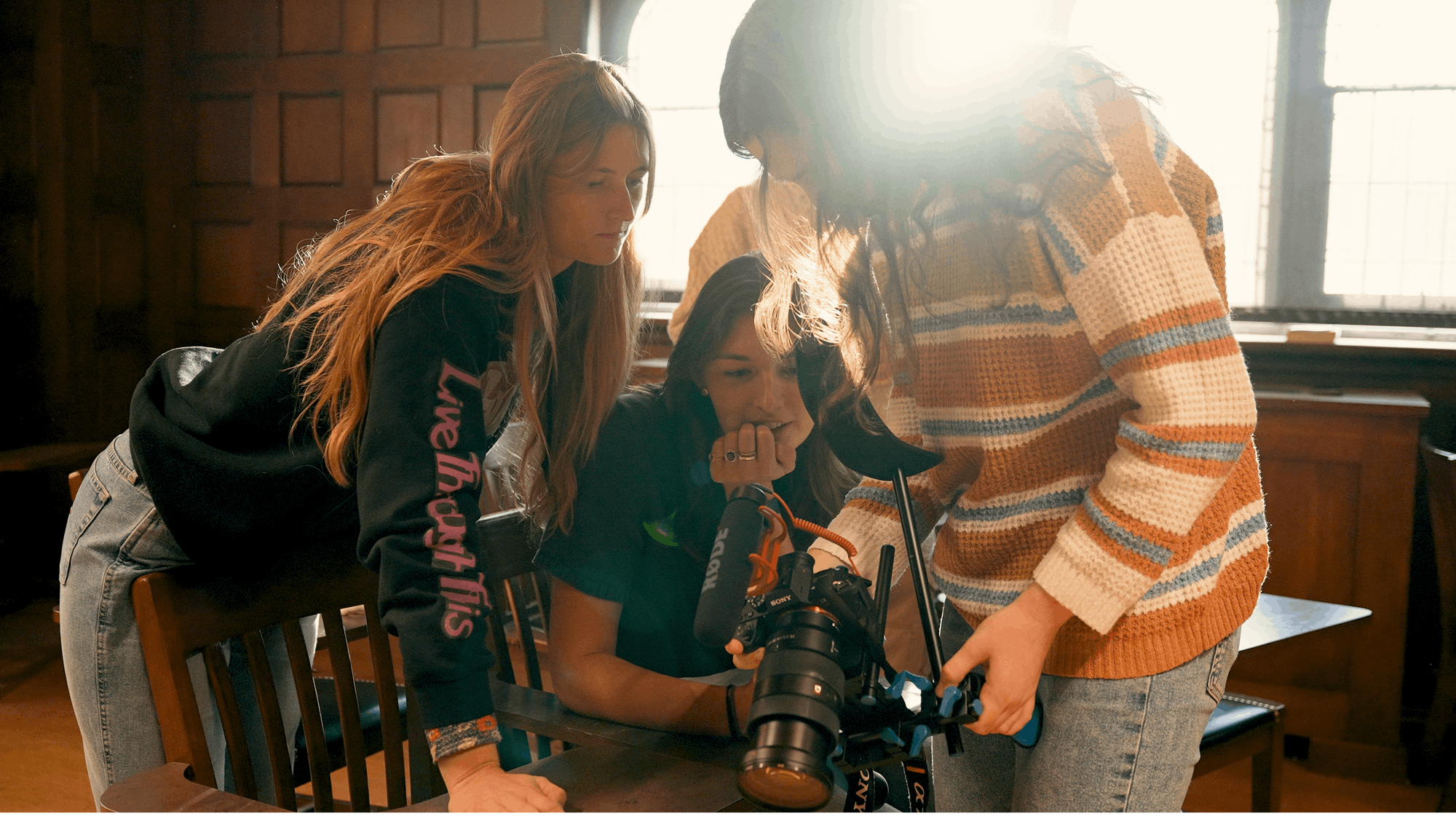 Three female students look at a recording in a camera.