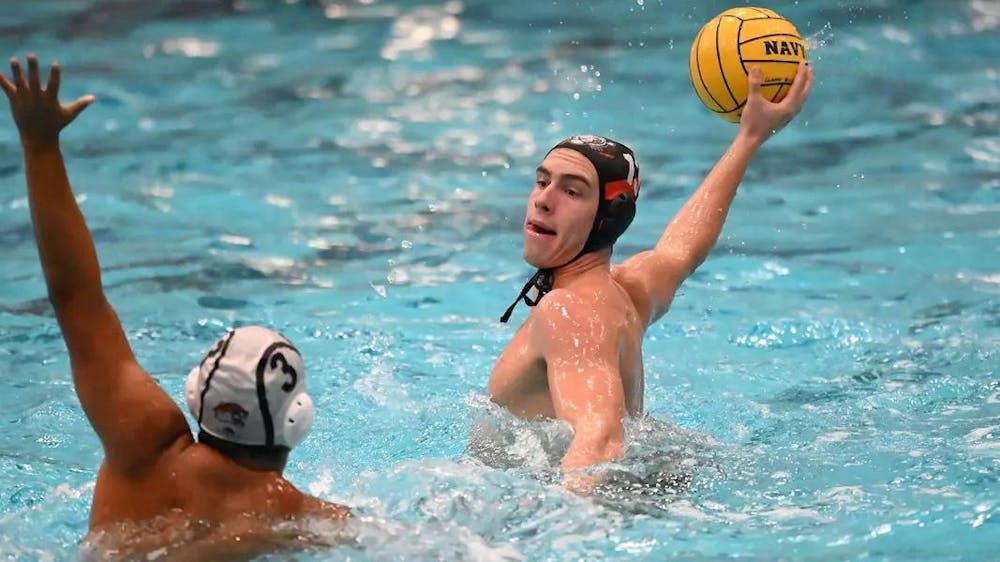 Male water polo player winding up to throw a yellow ball past opposing player.