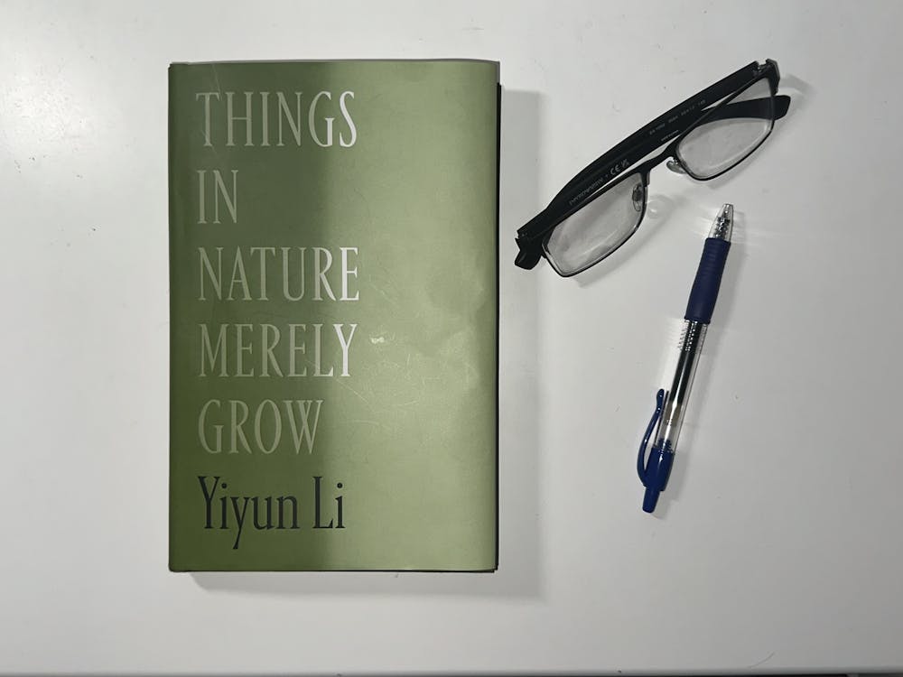 A green book with white letters that read "Things in Nature Merely Grow." There is a pair of black glasses and a black pen scattered next to the book. The items are all on a white background.
