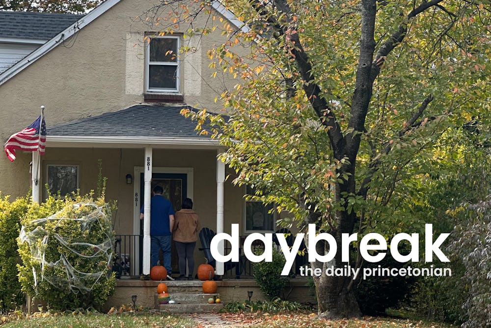 Two figures stand on the porch of a small brown house, looking away from the camera. The house has decorations for Halloween, including pumpkins and spiderwebs. In the foreground, text reads "Daybreak daily princetonian."