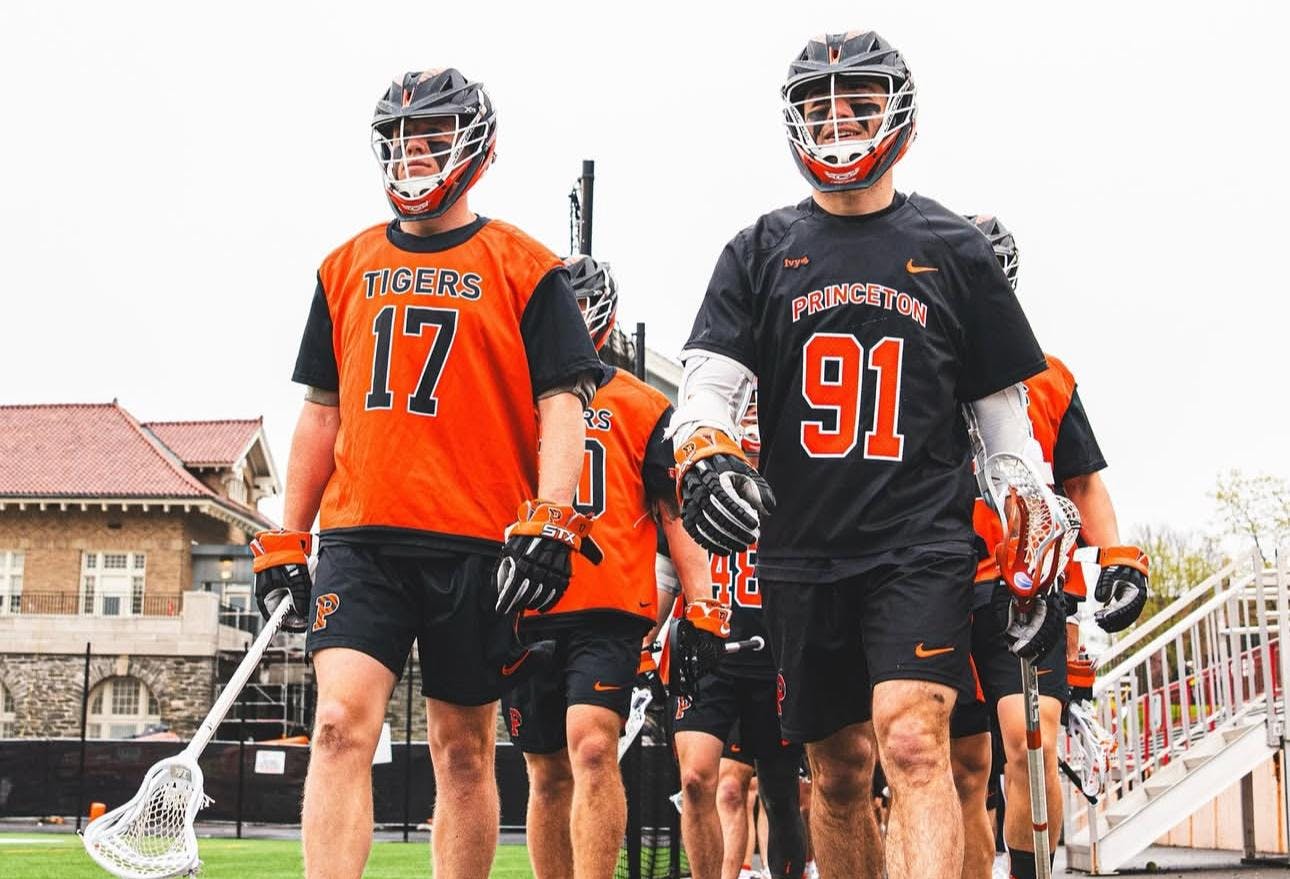 A group of men wearing orange and black jerseys walking on a grass field. 