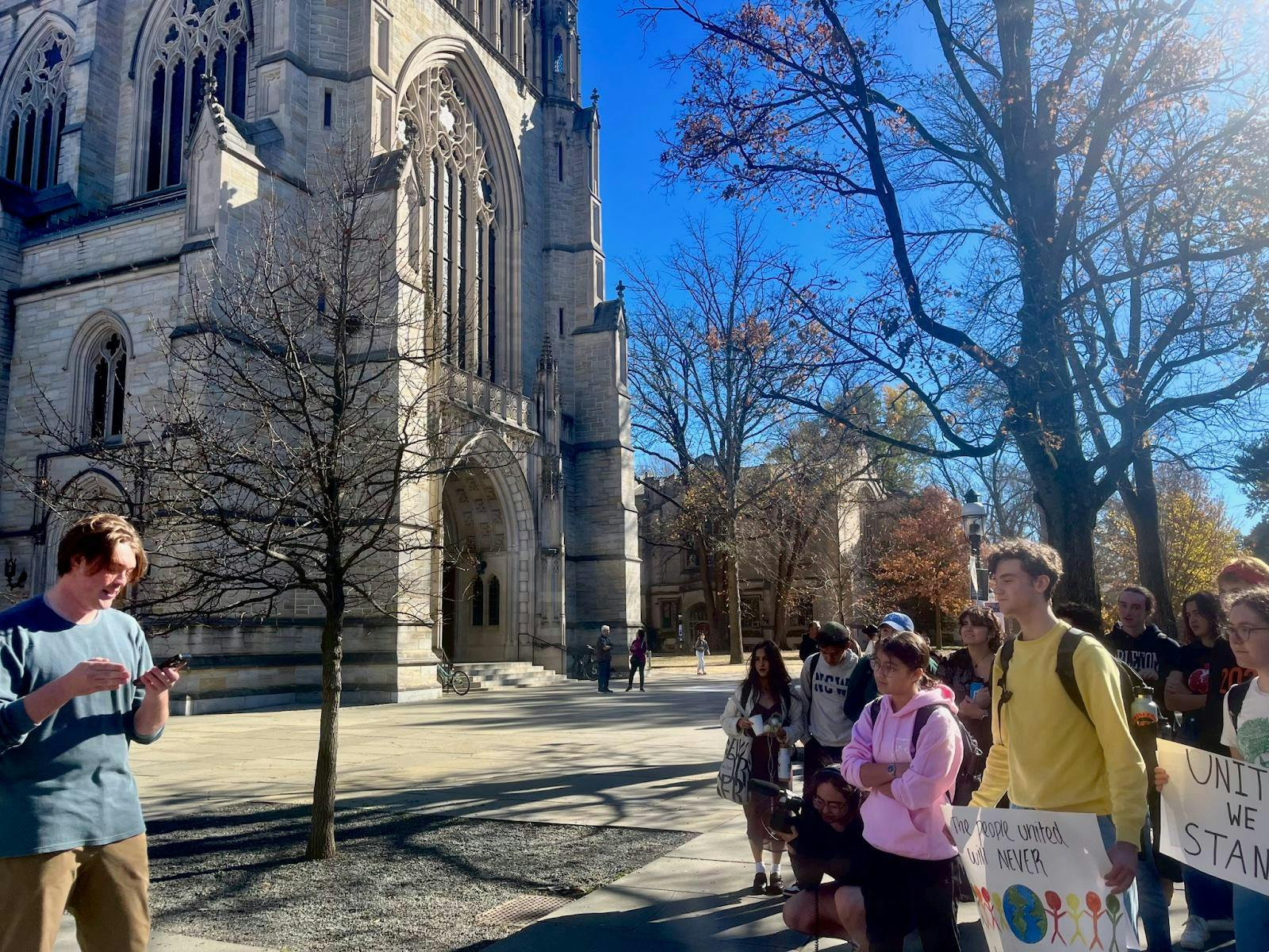 Group of students with sign standing outside a large stone Chapel. 