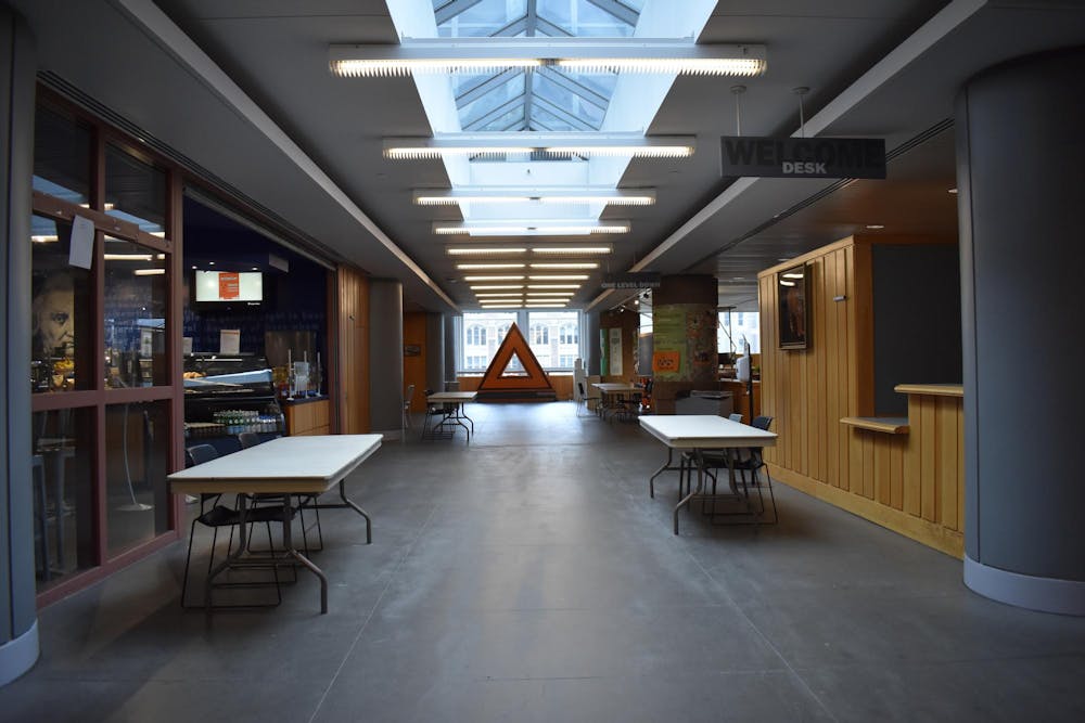 There is an empty hallway lined with folding tables, with fluorescent lighting overhead.