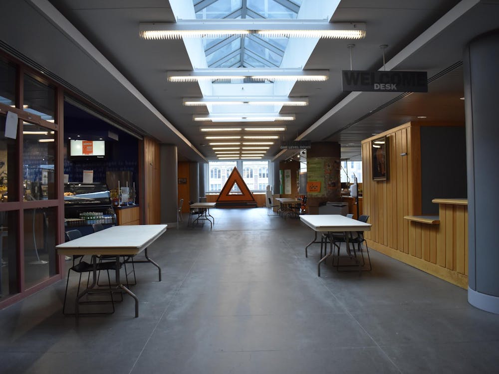 There is an empty hallway lined with folding tables, with fluorescent lighting overhead.