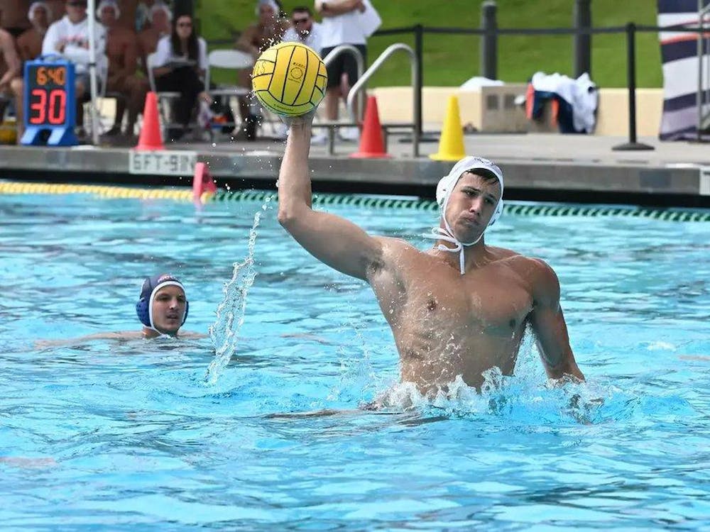 Man wearing white swim cap in pool hitting a yellow water polo ball.