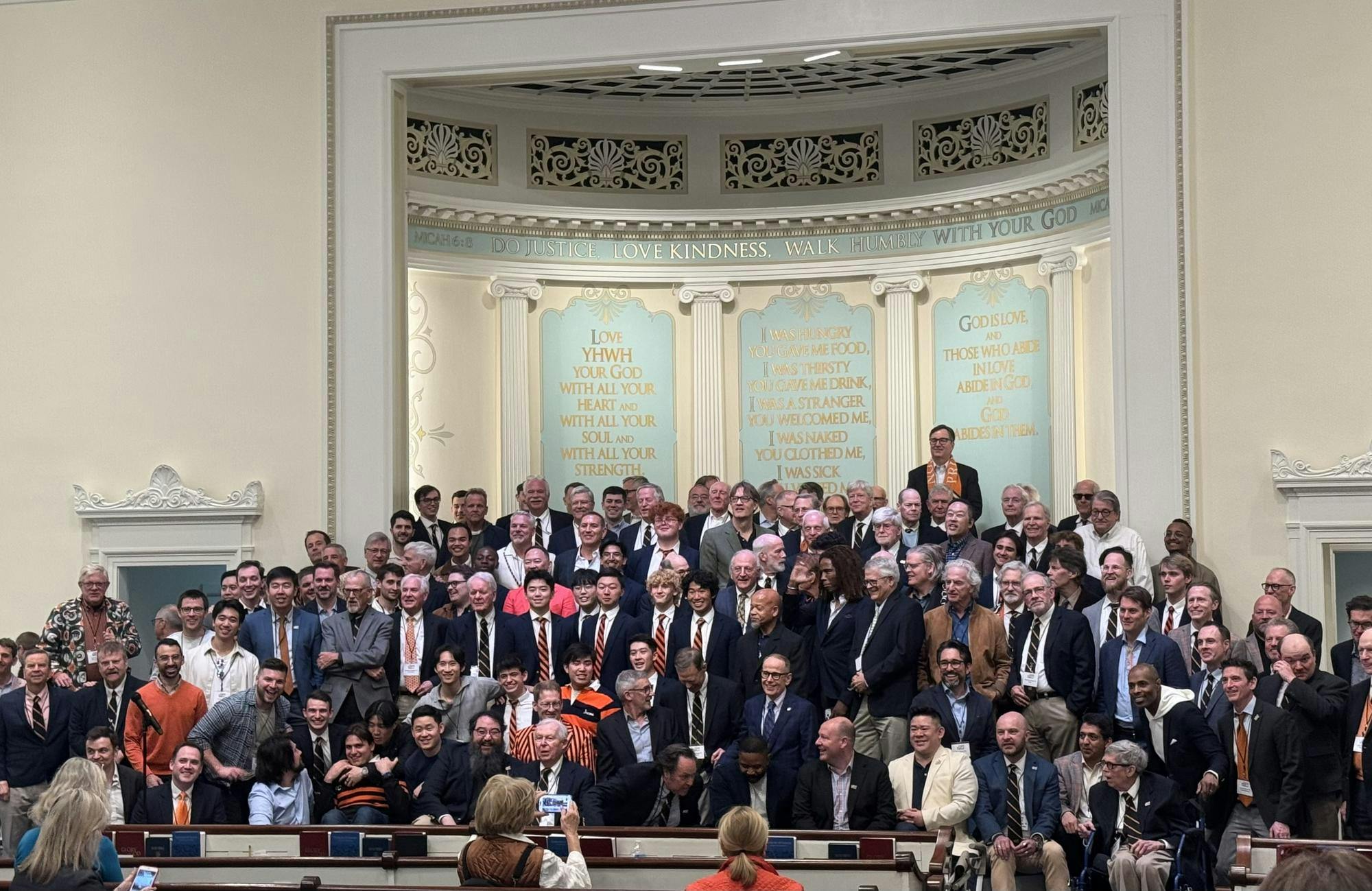 Several dozen people of all ages are standing together on a stage in outfits of many different colors and styles.