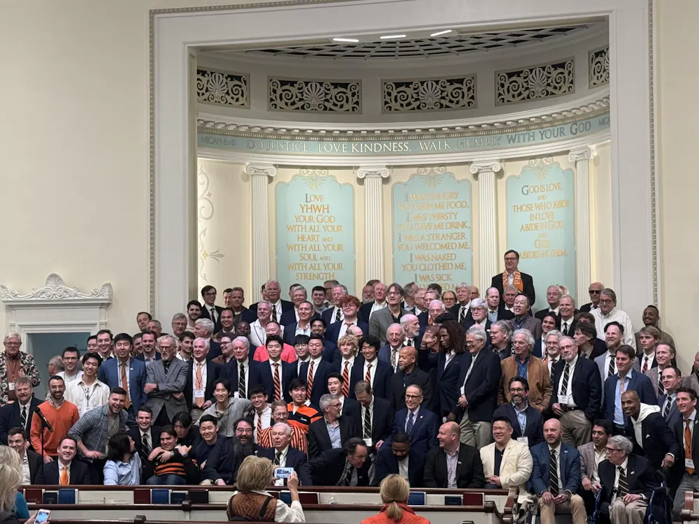Several dozen people of all ages are standing together on a stage in outfits of many different colors and styles.