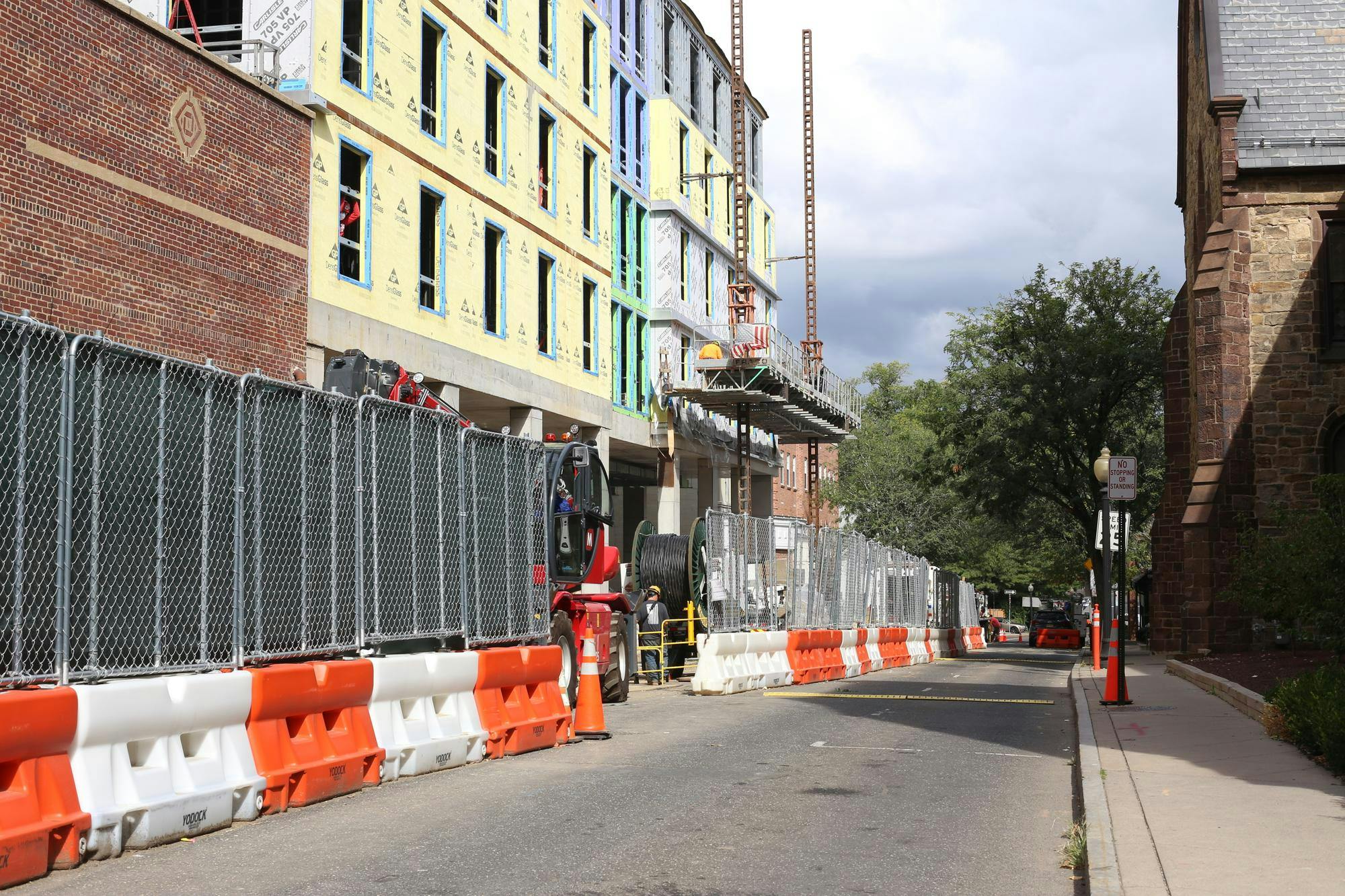 Orange and white barriers block off one half of a street, with a partially-constructed building in the background
