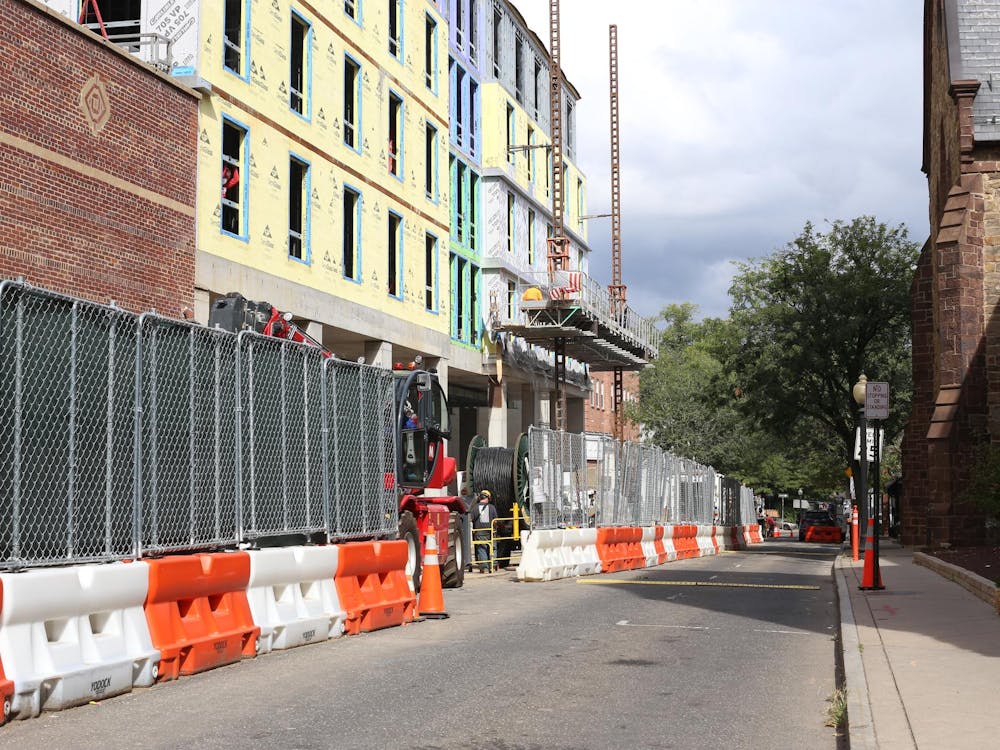 Orange and white barriers block off one half of a street, with a partially-constructed building in the background
