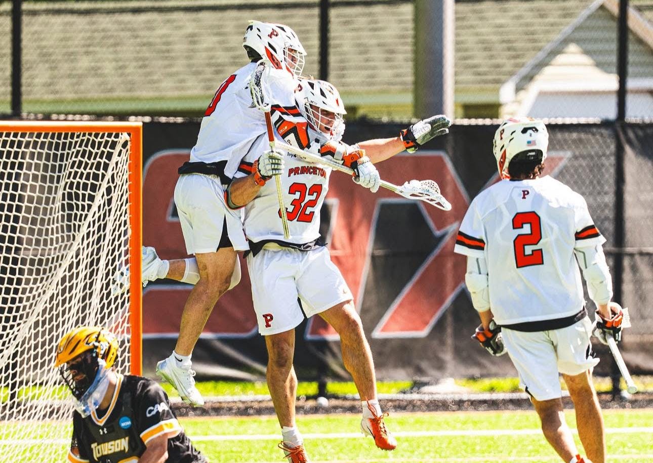 Three players wearing white shorts and white jerseys celebrating on a grass field after a goal. 