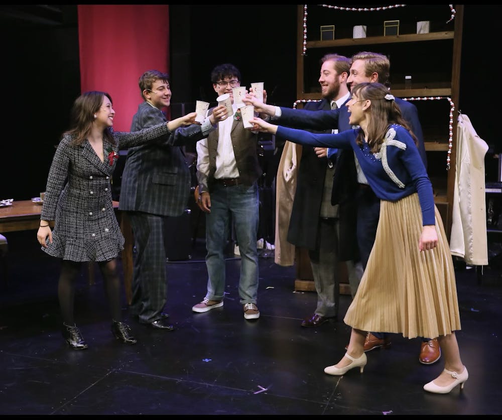 A group of actors clink glasses onstage.