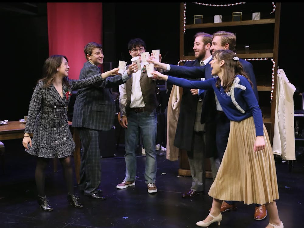 A group of actors clink glasses onstage.