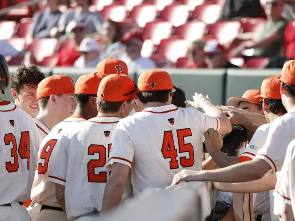 Princeton baseball players in white jerseys and orange baseball hats put their hands in a circle for a team chant.
