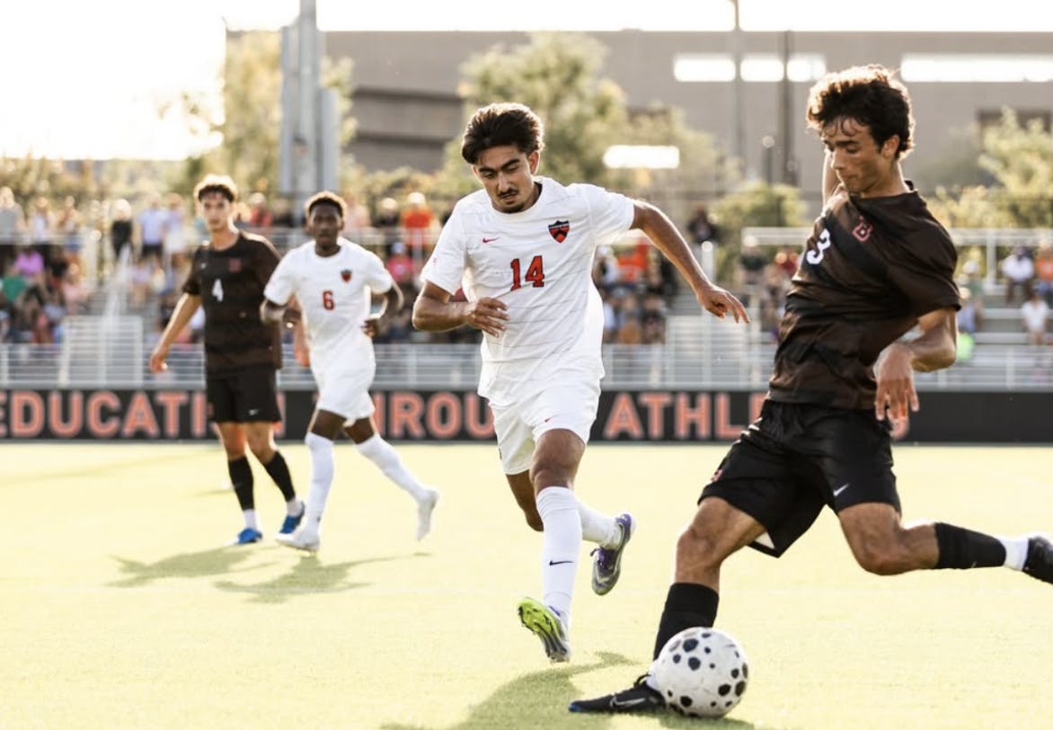 A soccer player wearing white keeps his eye on the ball while sprinting past a defender wearing black.