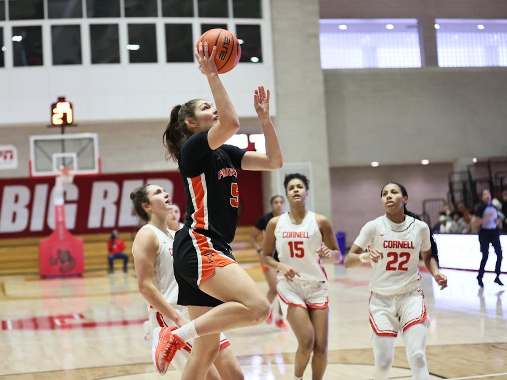 Player in orange and black jumps to attempt a layup with three defenders in white uniforms looking on. 