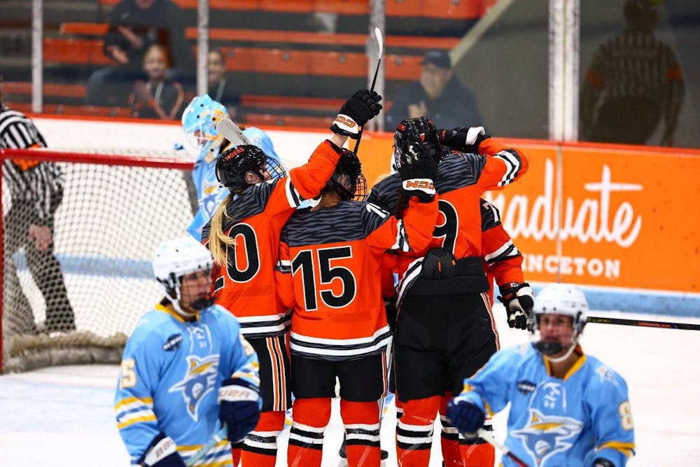 Three women in orange jerseys playing hockey celebrate with their teammate