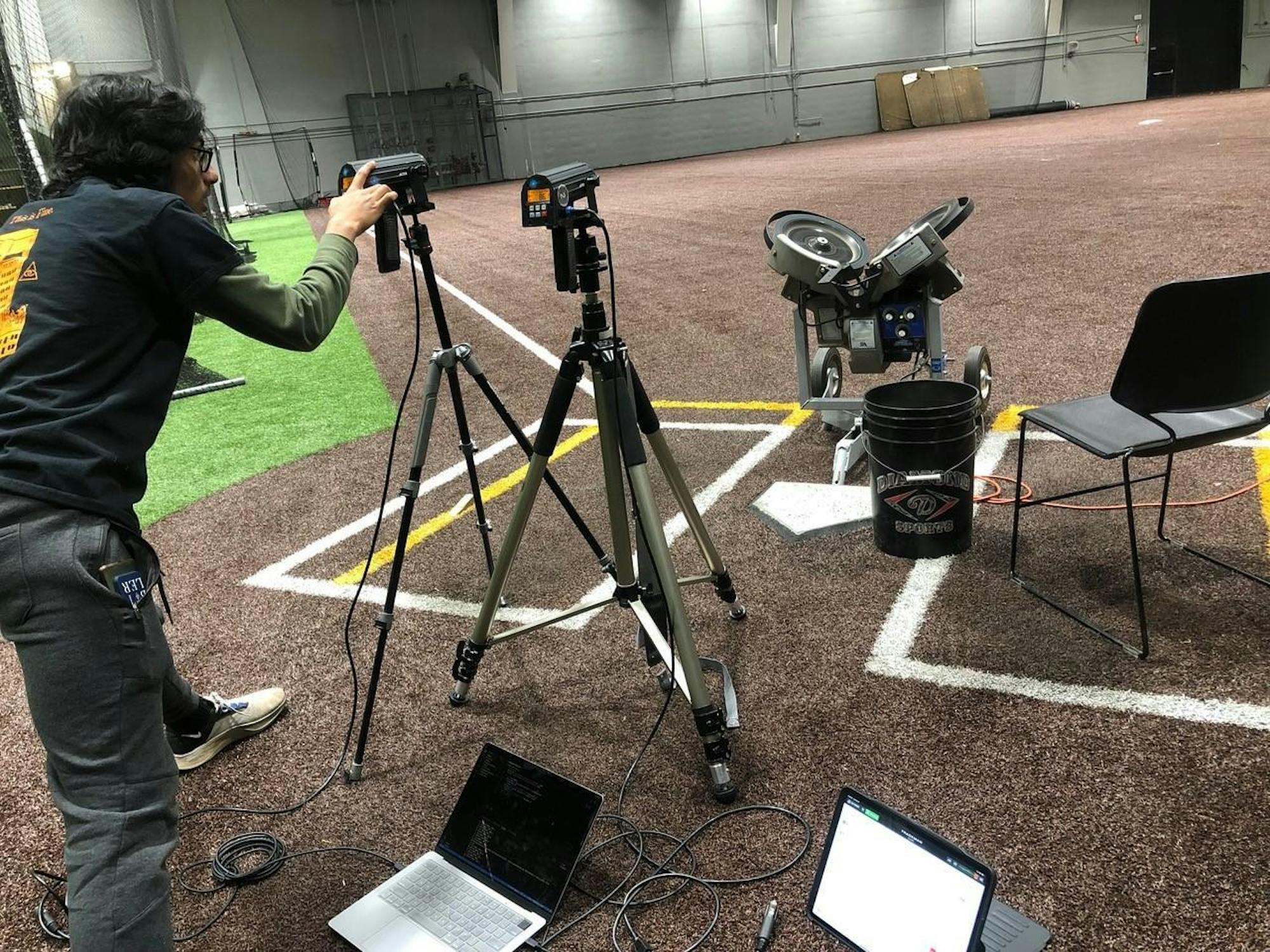 A man working with analytical equipment inside an indoor baseball practice arena. 