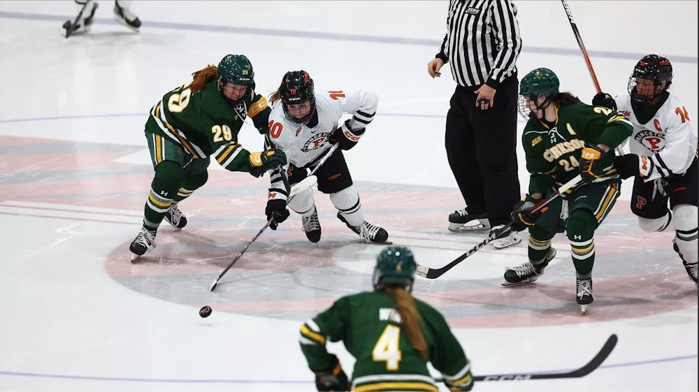 A woman in a white jersey skates through a crowd of defenders in green jerseys