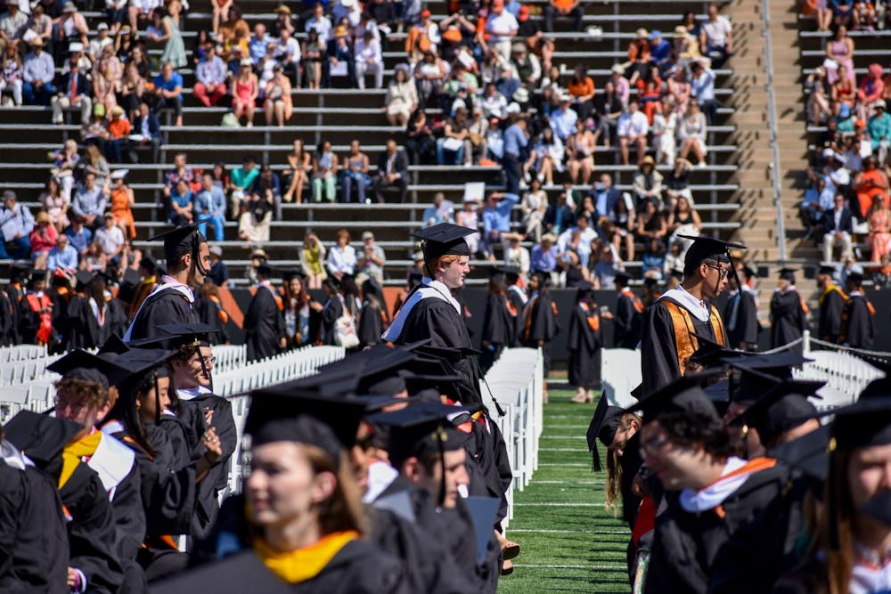 Students in academic regalia march into stadium joining other students already seated.