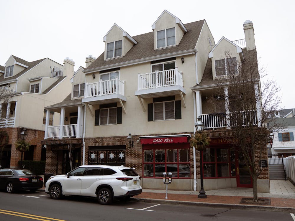 Cars line a street in front of the facade of a white-yellow building.