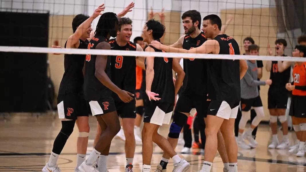 Six players in orange and black huddle together after winning a point. 