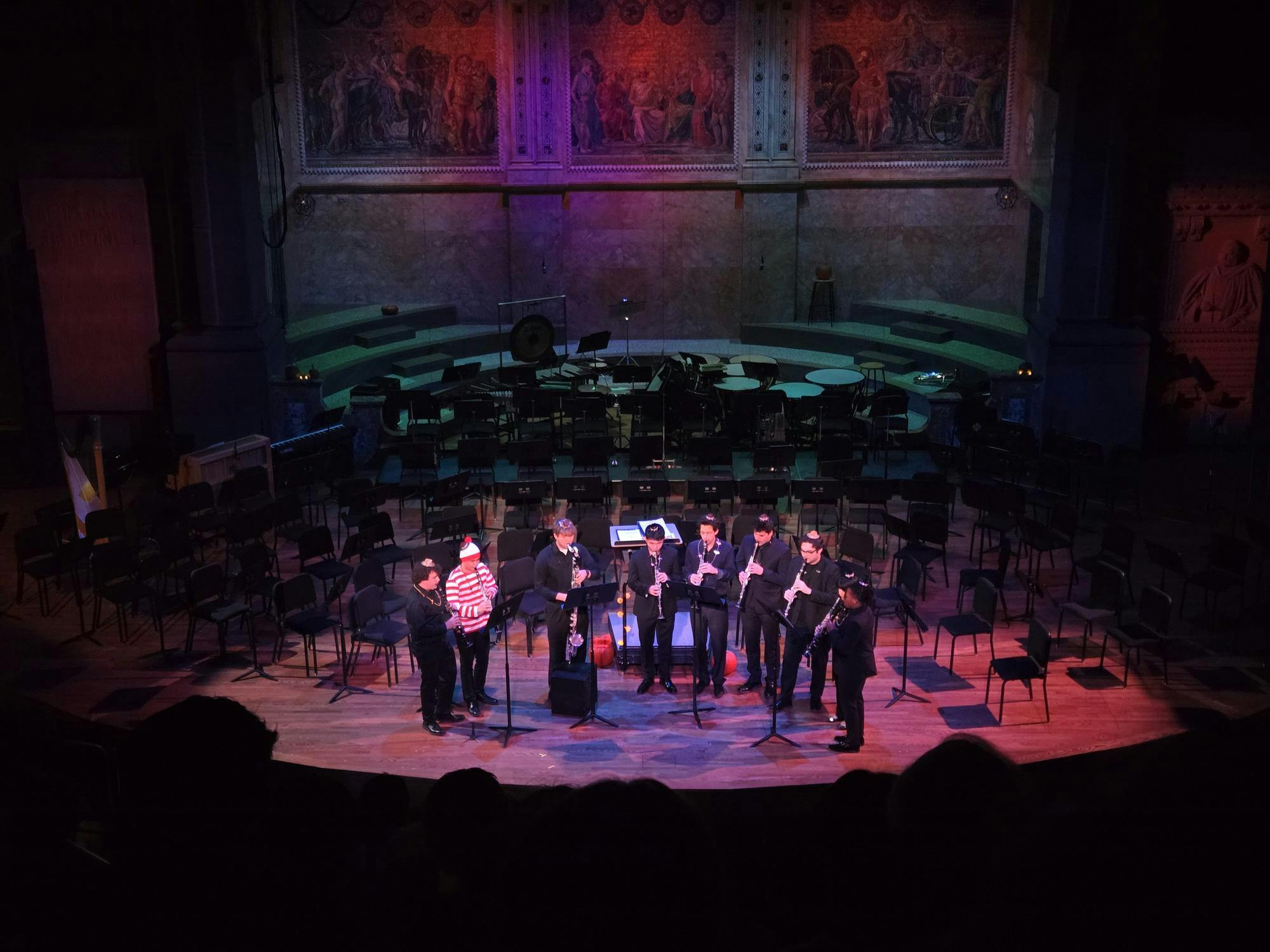 Nine clarinet players standing in a semicircle on stage.