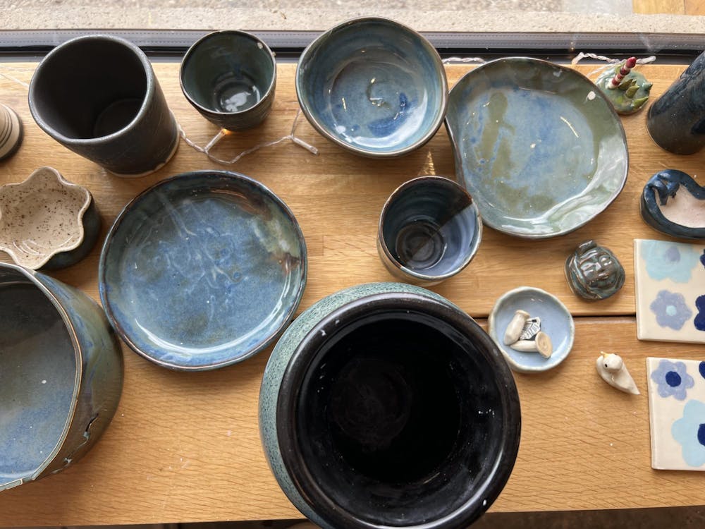 An assortment of ceramics including cups, bowls, and plates in various hues of blue sit on a wooden ledge.