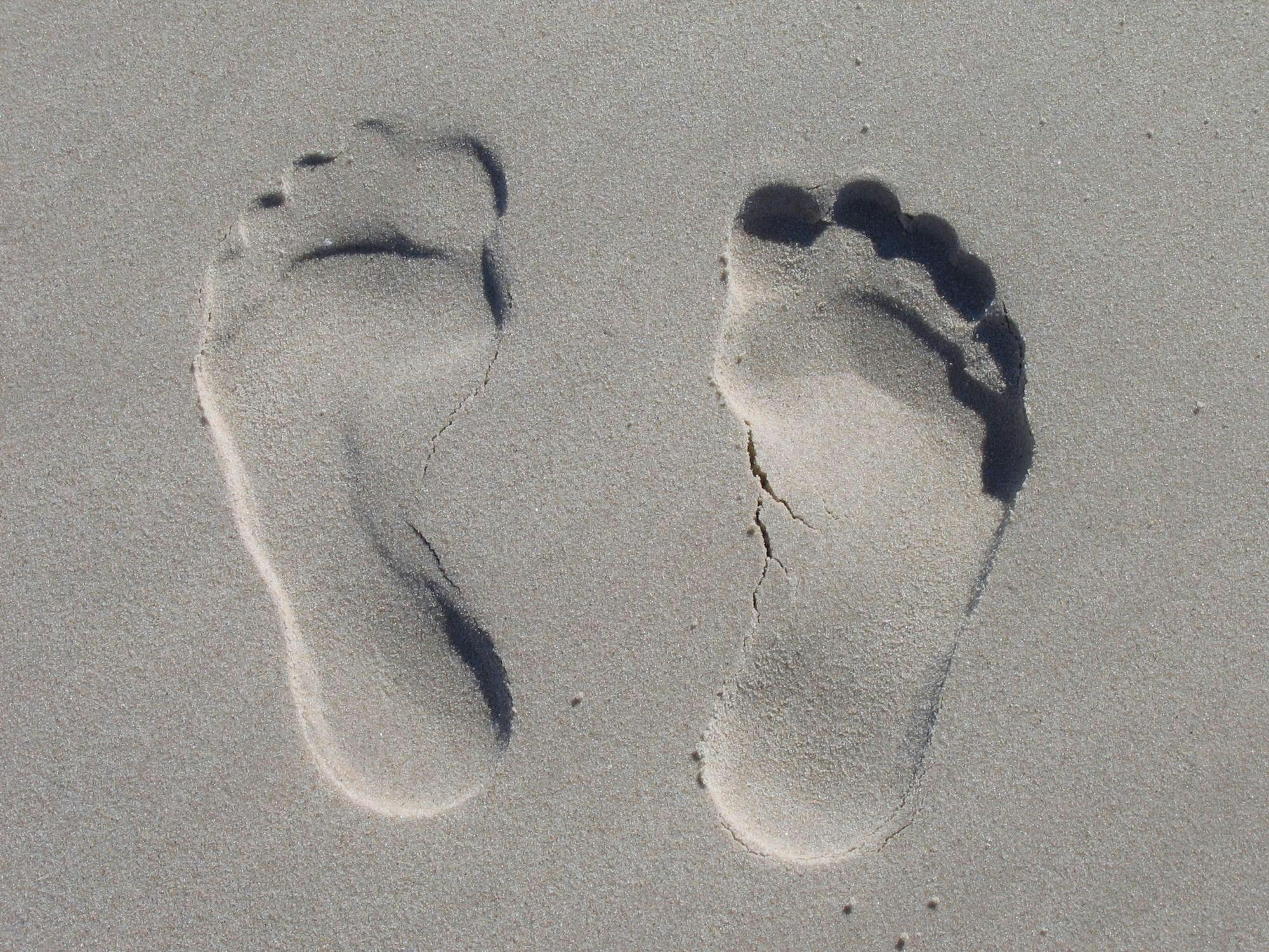 Two footprints in gray sand, with the left slightly more forward and shallow than the right
