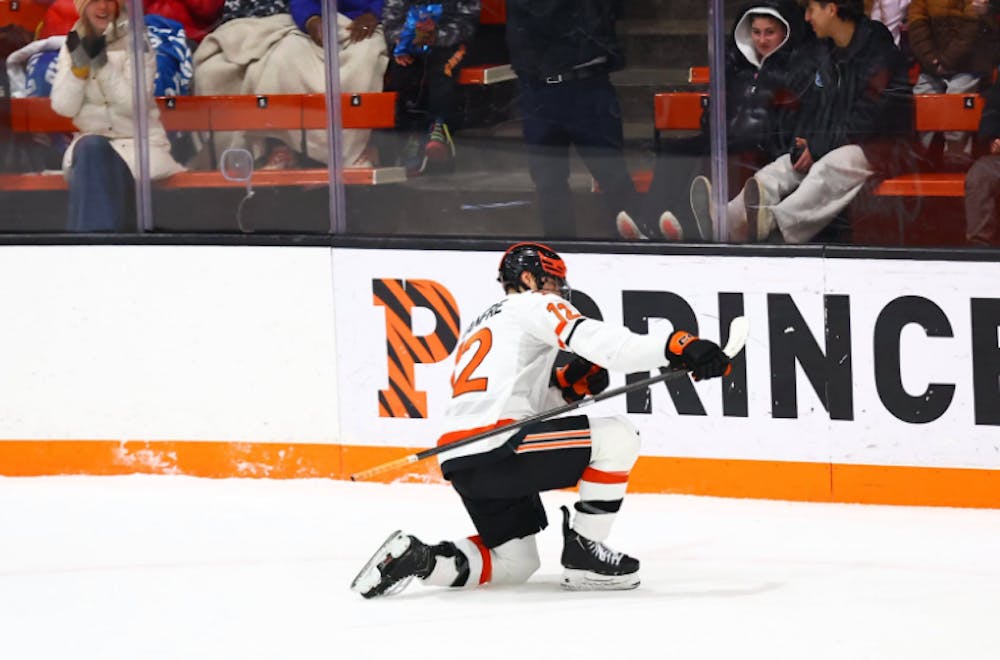A Princeton player in a white jersey celebrates a goal by sliding on one knee with his stick in his right hand
