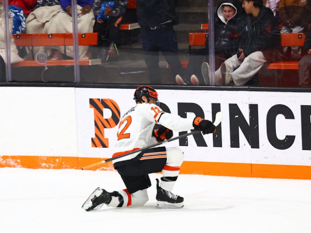 A Princeton player in a white jersey celebrates a goal by sliding on one knee with his stick in his right hand