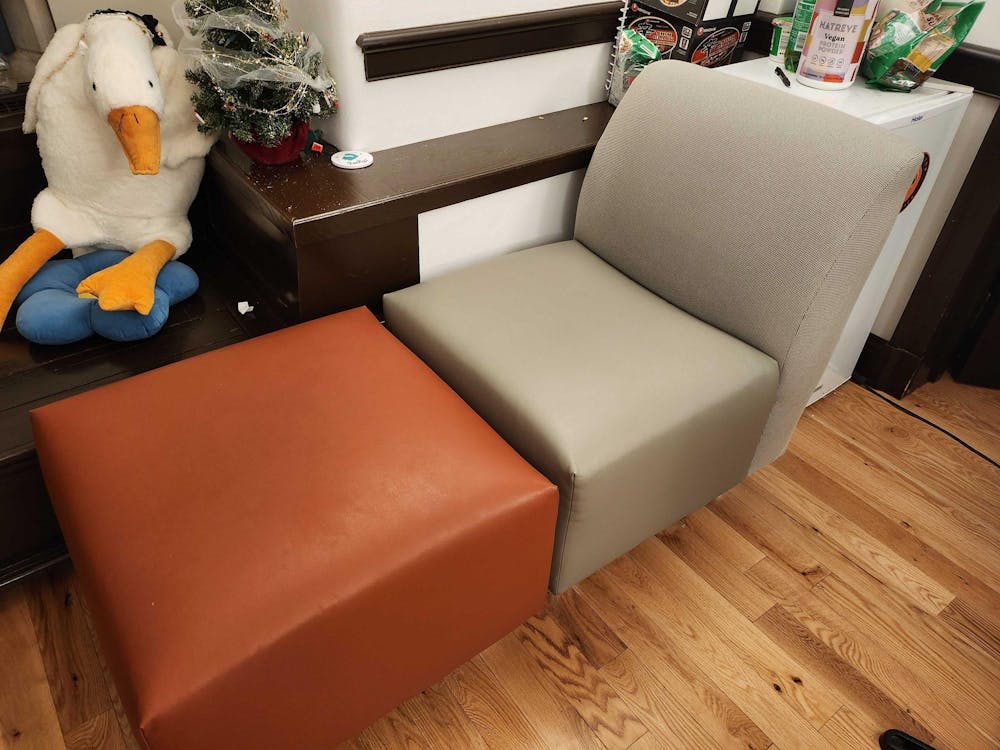 An orange ottoman and a grey chair on a brown wooden floor are featured in the photo.