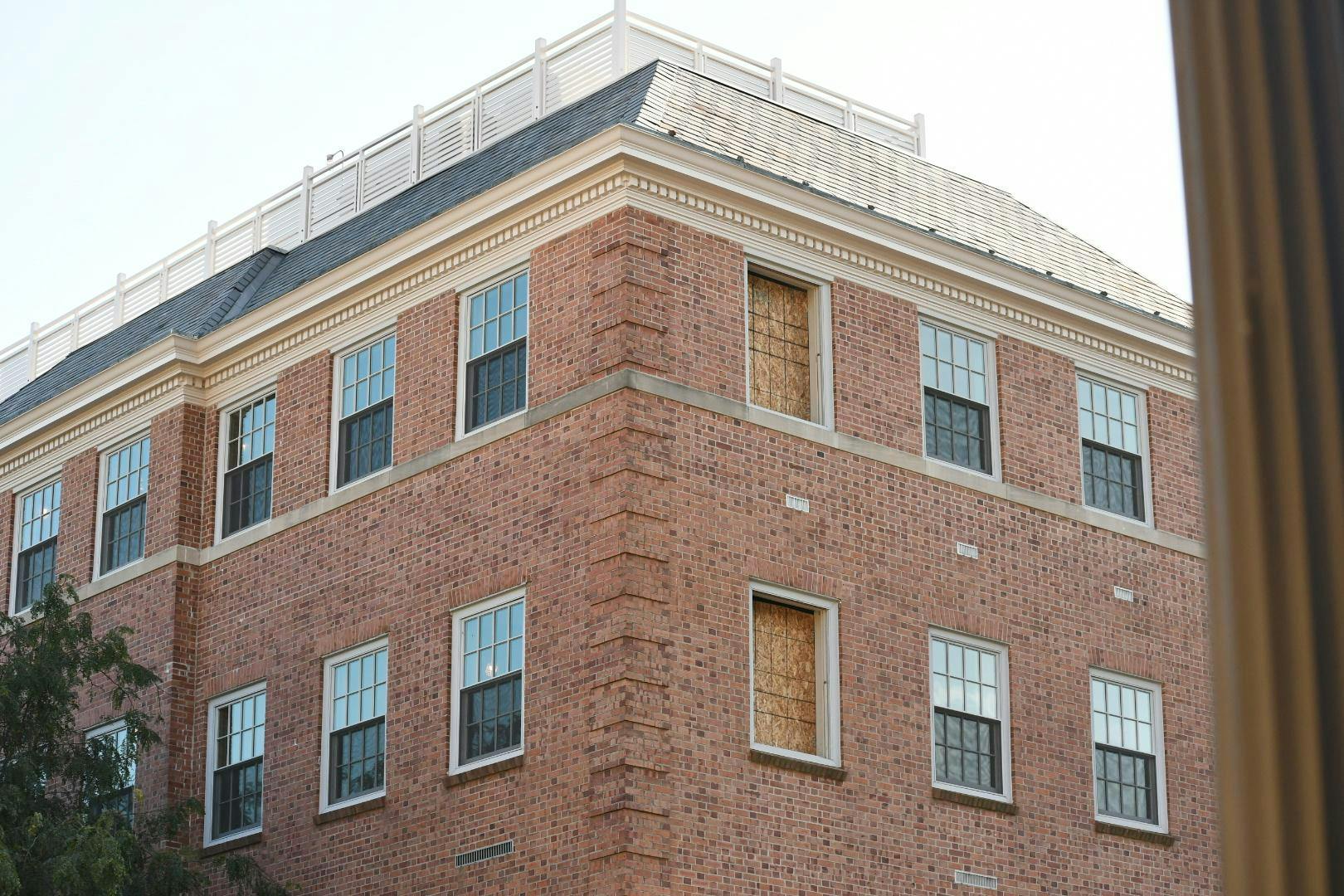A big square red brick building with windows captured from an angle. &nbsp;Two windows are missing and there is wood over them