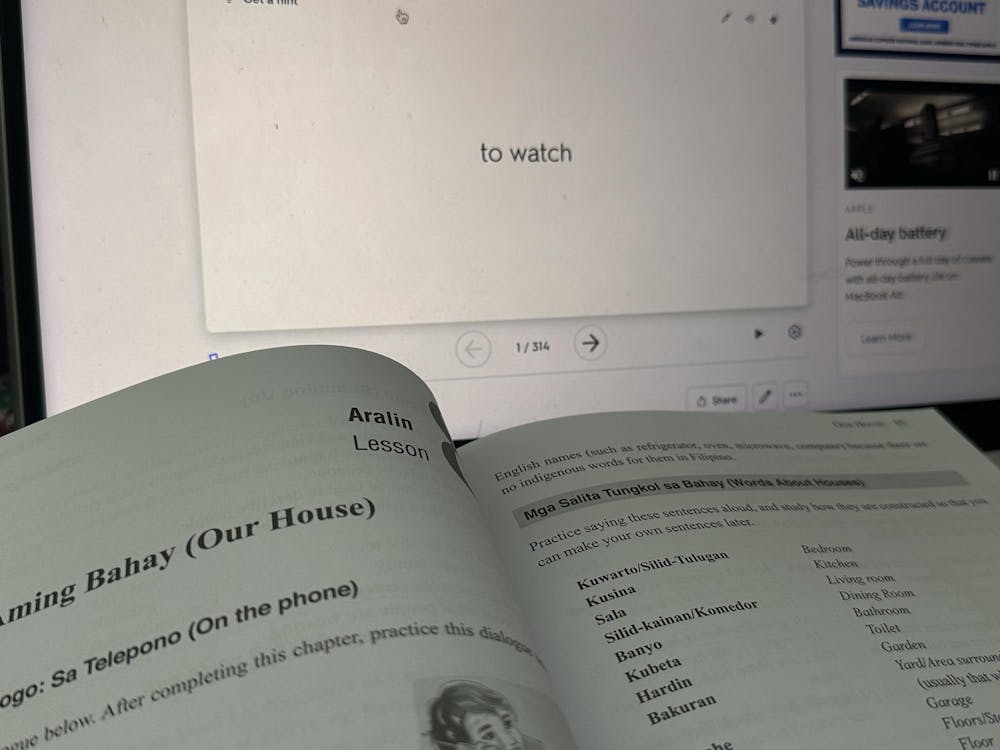 A grammar textbook in front of a flashcard on a laptop defining “to watch.”