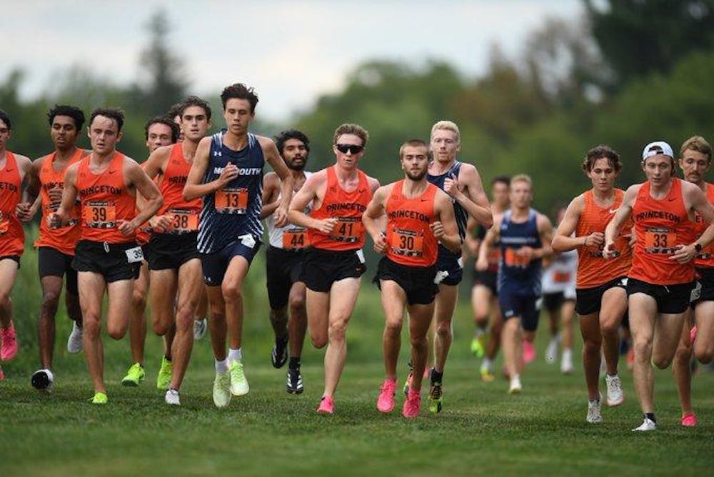 Men in orange jerseys and blue jerseys race in a cross country meet.