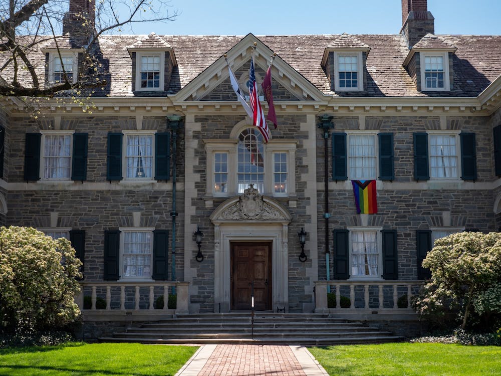 A stone building with a wooden door and multiple windows. There are four flags on the building, including the American flag and the LGBTQ+ flag.