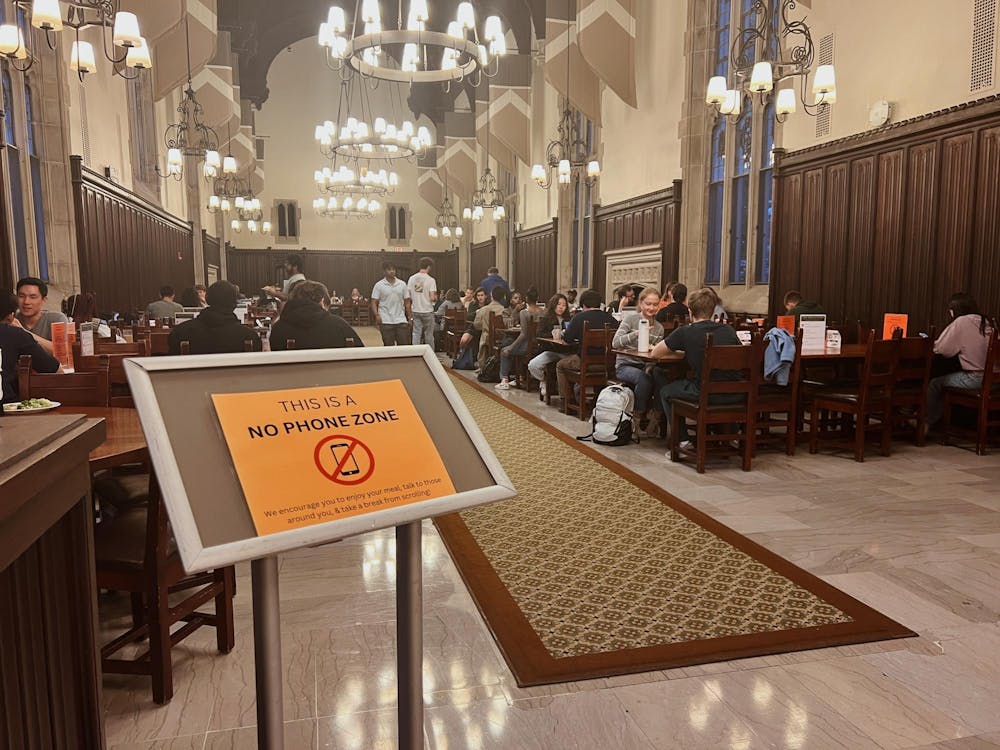 People eat at a row of wooden tables, with a sign in the foreground that reads, "this is a no phone zone"