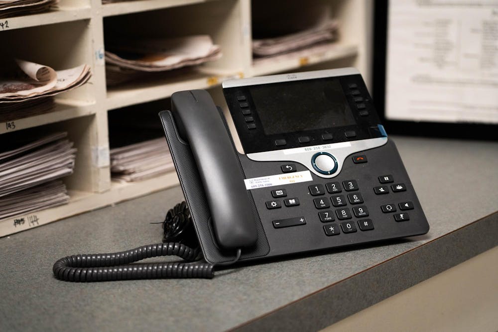A Cisco VoIP phone sits on a desk. Cubbies filled with stacks of papers stand in the background. 