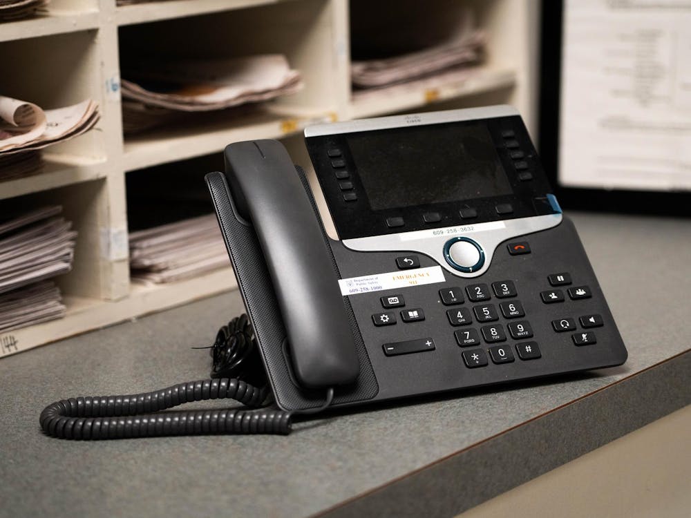 A Cisco VoIP phone sits on a desk. Cubbies filled with stacks of papers stand in the background. 