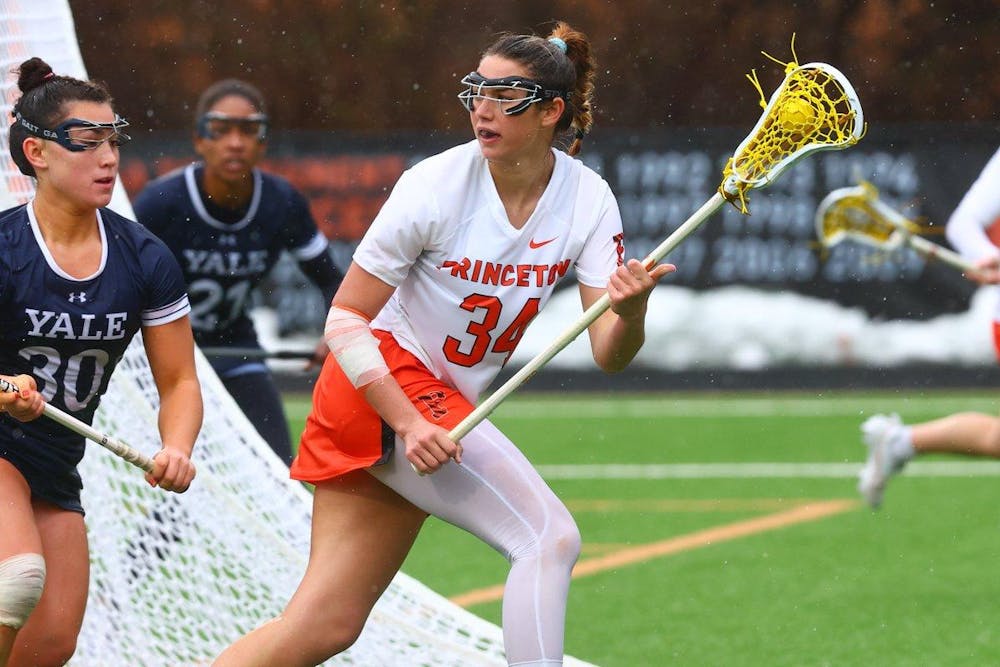 Woman in Princeton uniform carries lacrosse ball and looks up the field. 