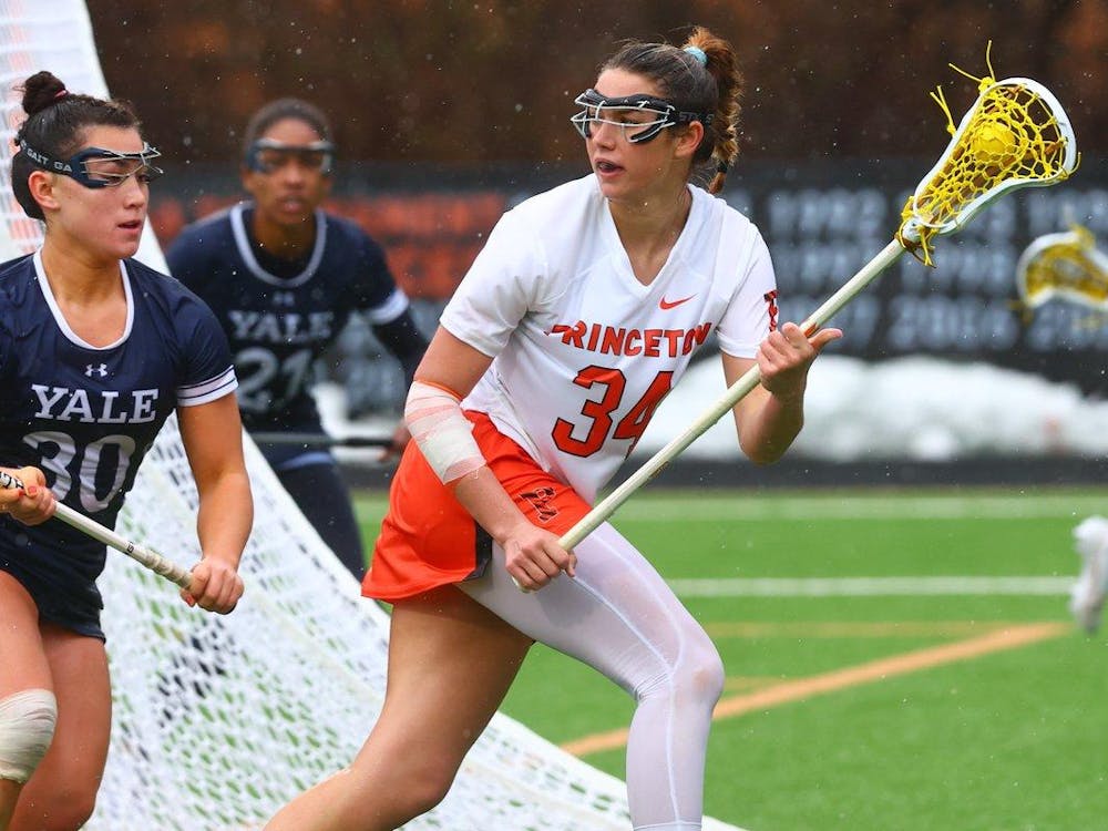 Woman in Princeton uniform carries lacrosse ball and looks up the field. 