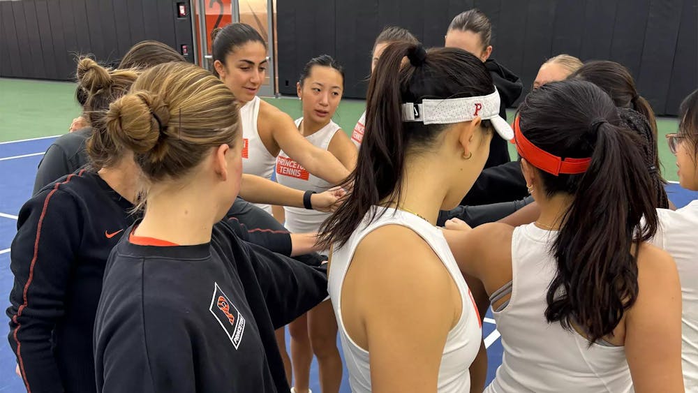 Women's tennis players huddle in a circle and put their hands in the middle. 