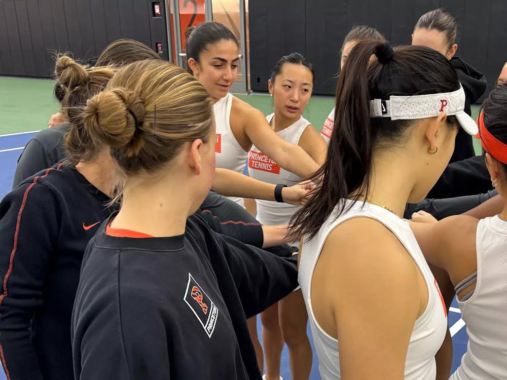 Women's tennis players huddle in a circle and put their hands in the middle.